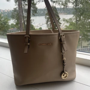 Beige Michael Kors tote väska - Äkta Michael Kors tote - i färgen sand. Mått 15x32x26 (bredd x längd x höjd). Rymmer en större laptop! Bra använt skick - få missfärgningar (på undersidan), perfekt inuti. Liten defekt på handtag (se bild). Köpt hos Michael Kors för ca 2500kr. Läder.
