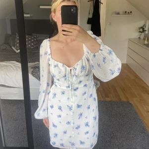 Mia Mini Dress- Gina tricot - Säljer denna vita klänning med små blå blommor på, helt oanvänd (prislapp kvar)! Stl.40, passar mig som brukar ha allt mellan 38-42! Den är stretchig över bröstet/magen och har ett under tyg vilket gör att den inte är genomskinlig!