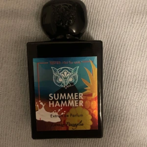 Summer Hammer Extrait de Parfum - En elegant flaska med svart lock och en färgglad etikett som pryds av en uggla. Parfymen heter Summer Hammer och är en Extrait de Parfum, vilket innebär en hög koncentration av doftoljor. Perfekt för den som vill ha en långvarig och intensiv doftupplevelse.