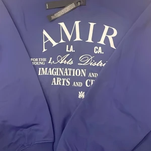  Amiri Hoodie  - Säljer en snygg blå sweatshirt från Amiri med tryck i vitt på framsidan. Tröjan har rund hals och långa ärmar, perfekt för en avslappnad stil. Den är i storlek medium och har en modern design med textdetaljer.