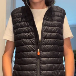 Svart dunväst från Save The Duck - Snygg svart dunväst från Save The Duck. skick 7/10 har knappt använt den med den har legat hemma i ett år och försöker nu sälja den. finns en annan annons på samma bilder och väst och det är jag som säljer denna. skriv för frågor eller funderingar 