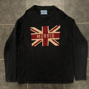 Svart tröja från Morris - Säljer en svart tröja från Morris med ett stort Union Jack-motiv och texten 'Morris' på framsidan. Tröjan är tillverkad i 100% bomull och har långa ärmar. Perfekt för en stilren och avslappnad look.