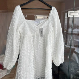 Vit blommig klänning från NA-KD - Säljer en vit klänning från NA-KD med blommigt mönster och puffiga långa ärmar. Klänningen är perfekt för vår och sommar. Den är tillverkad i ett lätt och luftigt material.