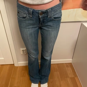 Blå bootcut jeans - Snygga blå bootcut jeans med klassisk femficksdesign och knappgylf. Perfekta för en avslappnad stil. De har en lätt tvättad look och är bekväma att bära.