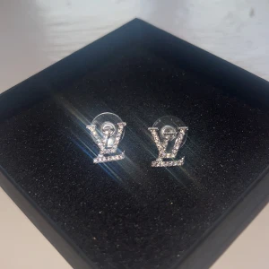 Glittriga silver örhängen med logo - Snygga örhängen i silver med en glittrig LV logga               Aldrig använda