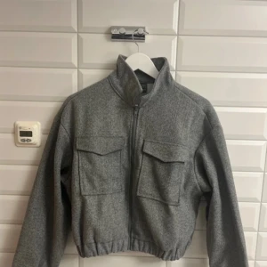 Grå jacka från Lypobala storlek:XL - Säljer en stilren grå jacka från Lypobala. Jackan har en dragkedja framtill och två stora fickor med lock på bröstet. Den är långärmad och har en elastisk nederkant för en bekväm passform. Perfekt för kyligare dagar.aldrig använd. Från lypobala. Storlek:XL. Säljer för 110 kronor.✨