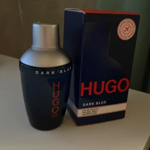 Hugo Dark Blue Eau de Toilette - Säljer en flaska Hugo Dark Blue Eau de Toilette. Flaskan har en elegant mörkblå design med silverfärgad kork och röd text. Perfekt för den som söker en sofistikerad och maskulin doft. Den är helt full och lådan är i perfekt skick. Hör av er vid funderingar.