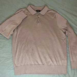 Beige pikétröja från Massimo Dutti - Säljer en stilren beige pikétröja från Massimo Dutti i mjuk merinoull. Tröjan har en klassisk krage med tre knappar och långa ärmar. Perfekt för en elegant och avslappnad look.OBS Dock ett deffekt är en liten fläck på framsidan.