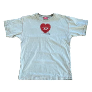 Taupe t-shirt med rött hjärta från Diesel - Säljer en taupe t-shirt från Diesel med ett stort rött hjärta. T-shirten är blekt på ett ställe, titta på den andra bilden!