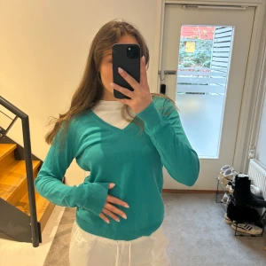 Turkos tröja med v-ringning - Säljer en snygg turkos tröja med v-ringning. Tröjan har långa ärmar och ribbade muddar vid ärmslut och nederkant. Perfekt för en avslappnad stil.