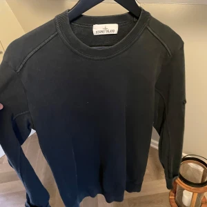 Svart långärmad tröja från Stone Island - Snygg svart långärmad tröja från Stone Island. Perfekt för en stilren och avslappnad look. Tröjan har en klassisk rund halsringning och är tillverkad i ett mjukt material. OBS patch är borta