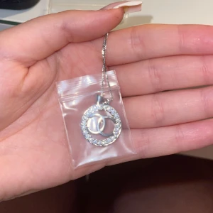 Silverfärgat halsband med glittrig cirkelberlock - Aldrig använd, pris går att diskutera. Elegant silverfärgat halsband med en glittrig cirkelberlock. Berlocken har en inre design med två sammanlänkade cirklar. Perfekt för att ge en touch av glamour till din outfit. 