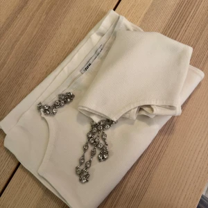 Vit kjol och top med  kedjedetaljer från Zara - Snygg vit kjol och top från Zara med unika kedjedetaljer. Toppen är ärmlös och har en stilren design som passar perfekt för en trendig look. Den är gjord i ett mjukt material som ger en bekväm passform. Har aldrig använt. PAKET PRIS