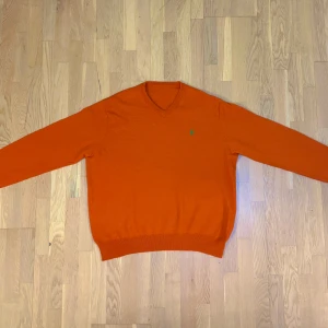 Ralph Lauren tröja - Säljer en snygg orange tröja från Ralph Lauren med en broderad grön logotyp på bröstet. Tröjan har en v-ringad hals, tröjan är storlek M men passar även L. Tröjan har nyligen blivit tvättad och inte bärts efter. Pris går att diskutera !