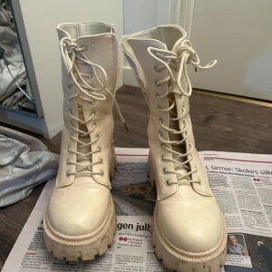 Beige boots med snörning och dragkedja - Snygga beige boots med grov sula och snörning framtill. De har även en praktisk dragkedja på sidan för enkel på- och avtagning. Perfekta för en trendig look.