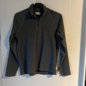 Moncler tröja - Snygg grå tröja från Moncler med halv dragkedja. Tröjan har långa ärmar och Moncler loggan på vänstra armen. Det är storlek 14 dvs 164. Passar den som är 155-165.