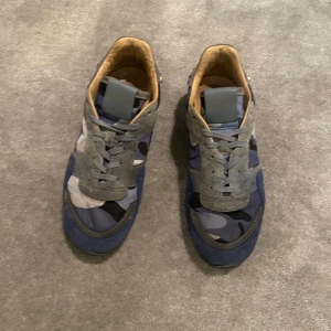 Valentino rockrunners - Snygga Valentino sneakers i blått och grått med ett coolt camouflagemönster. Skorna har snörning och är dekorerade med nitar runt hälen. Perfekta för en trendig look.