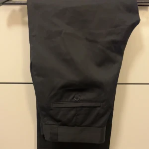 Svarta kostymbyxor - Snygga svarta kostymbyxor med en klassisk design. Byxorna har en rak passform och är perfekta för en stilren look. De har fickor och en knappdetalj baktill. 