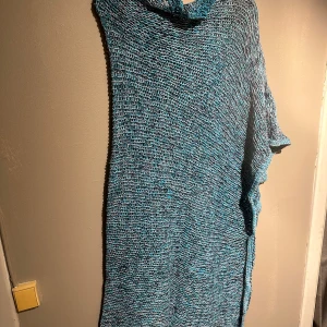 Blå stickad poncho  - Säljer en unik blå stickad poncho med en lös passform. Ponchon har en asymmetrisk design och är perfekt för en avslappnad stil. Den är tillverkad i ylle och silke som är ett mjukt och bekvämt material som ger en skön känsla.