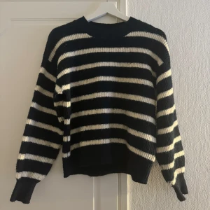 Svart och vit randig stickad tröja - Säljer en snygg svart och vit randig stickad tröja med långa ärmar. Perfekt för kyligare dagar och ger en stilren look. Tröjan har en klassisk design med ribbade muddar vid ärmslut och nederkant.