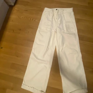 Vita vida byxor - Snygga vita byxor med hög midja och vida ben. Perfekta för en stilren look. Byxorna har en enkel design med knapp och dragkedja framtill.