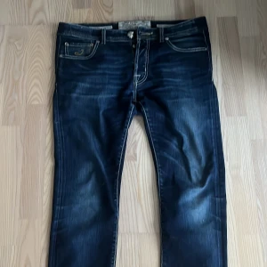 Mörkblå jeans från Jacob Cohen - Snygga mörkblå jeans från Jacob Cohen med kontrastsömmar och klassisk femficksdesign. Byxorna har en dragkedja och knapp framtill samt en läderpatch med logotyp baktill. Perfekta för en stilren look.