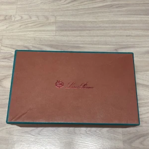 Svarta mockaloafers från Loro Piana - Eleganta svarta loafers i mjuk mocka från Loro Piana. Skorna har en stilren design med en dekorativ gulddetalj framtill. Fick dom av farsan, har använt de en gång på ett bröllop nu kommer de inte till användning mer går ner i pris vid snabb affär!