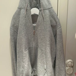 Grå hoodie från Weekday - Säljer en stilren grå hoodie från Weekday i storlek M. Den har en dragkedja framtill och en mysig huva med snörning. Perfekt för en avslappnad look.