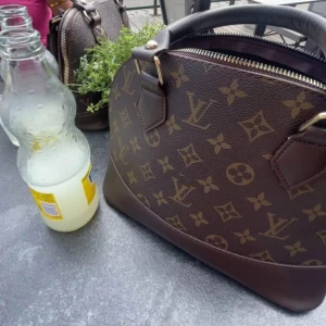 Brun handväska med monogram - Snygg brun handväska med klassiskt monogrammönster och dragkedja. Perfekt för att ge en lyxig touch till din outfit.