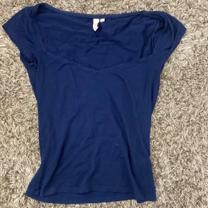 Mörkblå topp från Nelly - Säljer en mörkblå topp från Nelly med korta ärmar och v-ringad hals. Toppen har en fin spetsdetalj längs halsringningen. 