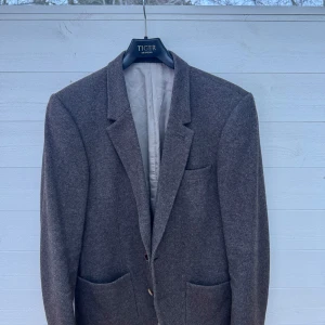 Brun kavaj från Tiger of Sweden - Snygg brun kavaj från Tiger of Sweden i klassisk design. Kavajen har två knappar framtill och är perfekt för en stilren look. Passar utmärkt till både formella och semi-formella tillfällen. Anledning till försäljning är pga utväxt. Storleken är 48 och sitter i slim fit