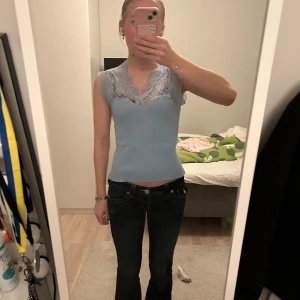 Blå ribbad topp med spetsdetaljer - Säljer en söt blå ribbad topp från Missäy med vackra spetsdetaljer vid halsringningen. Toppen är ärmlös och har en elegant v-ringad design. Väldigt vacker och använt ett fåtal gånger. 🩷