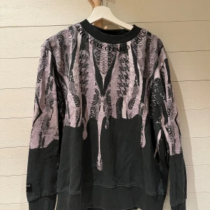 Mönstrad tröja från Carlo Colucci - Säljer en unik och stilren tröja från Carlo Colucci med ett abstrakt mönster. Tröjan har långa ärmar och en rund halsringning med textdetaljer. Storlek L. Skick 9/10.