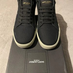 Svarta sneakers från Saint Laurent - Snygga svarta sneakers från Saint Laurent med vit sula och diskret logga på sidan. Skorna har snörning och är perfekta för en stilren look.