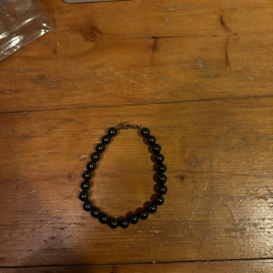 Svart pärlhalsband - Elegant svart pärlhalsband med glänsande pärlor. Perfekt för att ge en stilren touch till din outfit. Halsbandet har ett enkelt lås i guldton.