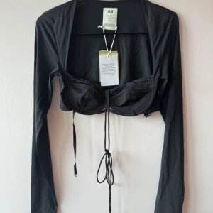 Svart långärmad bolerotopp från H&M - Snygg svart bolerotopp från H&M med långa ärmar och knytband framtill. En stilren touch till din outfit! Oanvänd med taggar kvar.