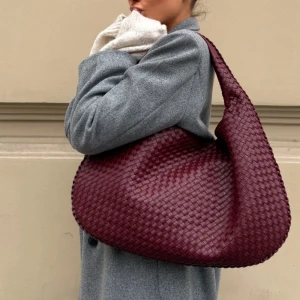 Vinröd axelväska i skinn - Snygg vinröd axelväska i flätat skinn med dragkedja. Perfekt för att ge en touch av stil till din outfit. Väskan har ett rymligt inre med plats för alla dina nödvändigheter.