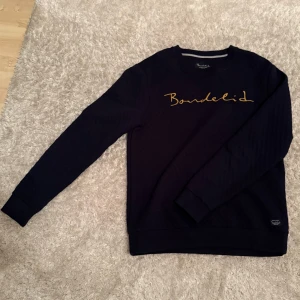 Svart tröja från Bondelid - Säljer en stilren svart tröja från Bondelid med gul text på bröstet. Tröjan har långa ärmar och en klassisk passform. Perfekt för en avslappnad look.