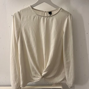 Vit blus från Vero Moda - Säljer en stilren vit blus från Vero Moda med långärmad design och en knutdetalj framtill. Blusen har en knappstängning i nacken🤍