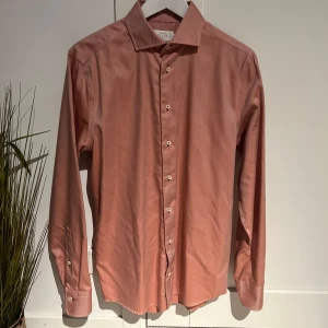 Röd randig skjorta från Riley - Snygg röd skjorta från Riley med diskreta ränder och klassisk krage. Skjortan har långa ärmar och knappar framtill. Perfekt för en stilren look.