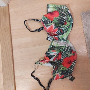  bikiniöverdel från Fantasie - Snygg bikiniöverdel från Fantasie med tropiskt blommönster i rött och grönt. Helt ny! Nypris var 599kr Är i storlek 85FF Den har justerbara axelband med prickigt mönster och är tillverkad i en mix av polyamid och lycra för en bekväm passform.
