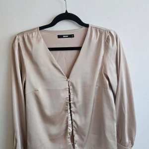 Satinblus i creme färg - Vacker satin blus med knappar framtill med V-ringning. 