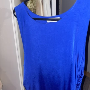 Blå klänning från WalG - Snygg blå klänning från WalG med draperad detalj på sidan. Perfekt för en elegant look. Klänningen har en enkel och stilren design.