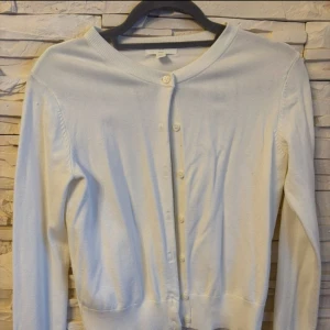 Vit kofta från H&M  - Säljer en stilren vit kofta från H&M Basics. Koftan har långa ärmar och knappar framtill. Den är tillverkad i ett mjukt material som ger en bekväm passform. 
