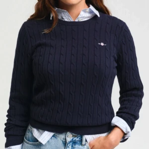 Mörkblå stickad tröja från Gant - Snygg mörkblå stickad tröja från Gant med kabelstickat mönster. Tröjan har långa ärmar och en rund halsringning. Perfekt för en stilren look. Köpt för ca 8 månader sedan för 1200 i johnells pch är använd ungefär 4 gånger.