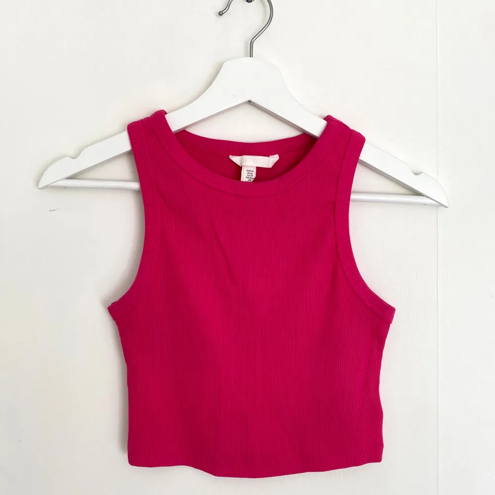 Snygg och trendig rosa ribbad linnetopp med croppad passform. Perfekt för en somrig look eller att styla med höga jeans. Toppen är ärmlös och har en enkel design som gör den lätt att matcha med olika outfits.. Yläosat.