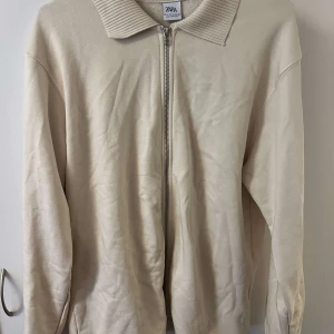 Beige tröja med dragkedja från Zara - Säljer en stilren beige tröja från Zara med dragkedja och krage. Tröjan har långa ärmar och är perfekt för en avslappnad look. Passar bra till både jeans och chinos.