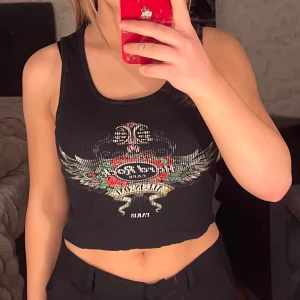 Svart ribbad linnetopp från Hard Rock - Snygg svart ribbad linnetopp från Hard Rock Café med tryck i flera färger. Toppen är croppad och ärmlös.