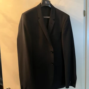 Svart kavaj och kostym byxor från SIR of Sweden  - Elegant svart kavaj från SIR i modellen Daniel. Kavajen har en klassisk design med två knappar framtill och en stilren passform. Perfekt för formella tillfällen. Du får även med SIR of Sweden kostym byxor. Storlek 148