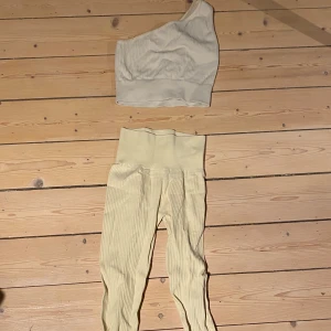 Beige ribbad oneshoulder topp och matchande underdel. - Snygg gul oneshoulder topp med ribbad struktur. Gjord för träning men perfekt för en stilren och modern look. Matcha med dina favoritjeans eller kjol för en komplett outfit. Matchande underdel tillkommer .